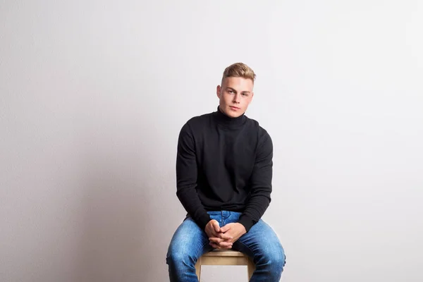 Porträtt av en ung man som sitter på en pall i en studio. Kopiera utrymme. — Stockfoto