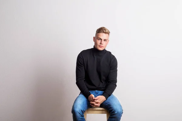 Retrato de um jovem sentado num banco de um estúdio. Espaço de cópia . — Fotografia de Stock