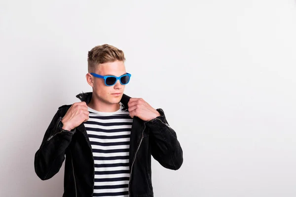 A confident young man with blue sunglasses in a studio, wearing striped T-shirt. — Stock Photo, Image
