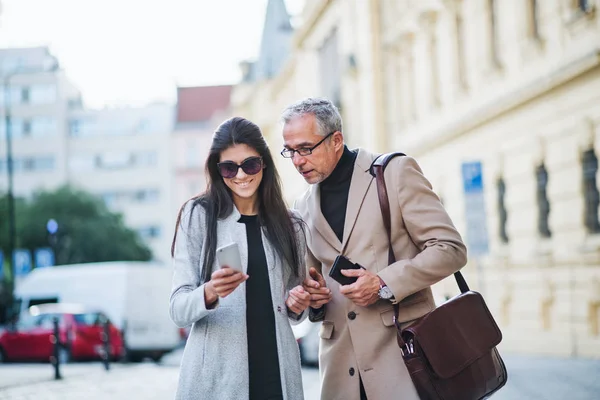 Hombre y mujer socios de negocios con smartphone de pie al aire libre en la ciudad, hablando . —  Fotos de Stock