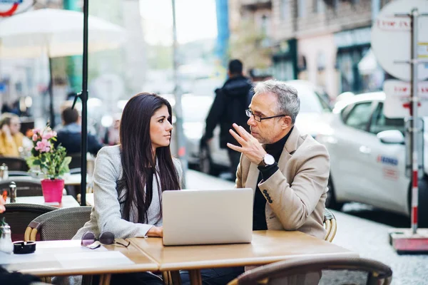 Homme et femme partenaires d'affaires avec ordinateur portable assis dans un café en ville, parler . — Photo