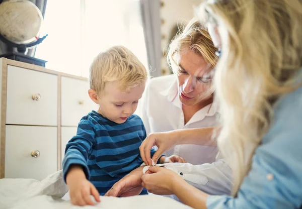 Jonge ouders met hun peuter zoon binnen in een slaapkamer, dressing. — Stockfoto