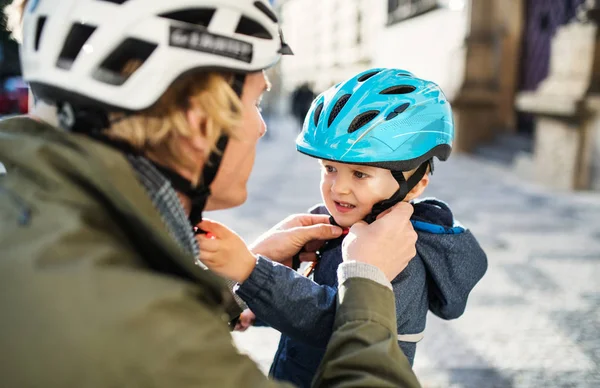 Ein junger Vater setzt seinen kleinen Söhnen im Freien in der Stadt einen Helm auf. — Stockfoto