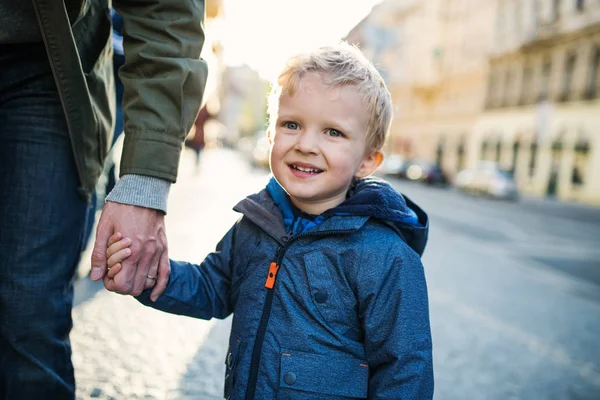 Een kleine peuter jongen met onherkenbaar vader buiten lopen in de stad. — Stockfoto