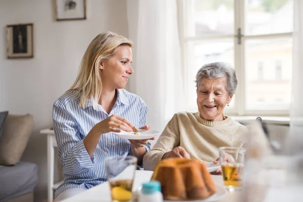 Donna anziana in sedia a rotelle con un visitatore di salute seduto a tavola a casa, mangiare . — Foto Stock