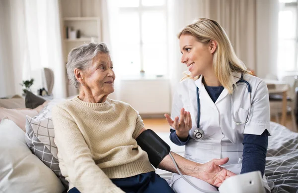 Visiteur de santé mesurant la pression artérielle d'une femme âgée à la maison . — Photo