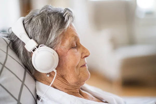 Kranke Seniorin mit Kopfhörern liegt zu Hause oder im Krankenhaus im Bett. — Stockfoto