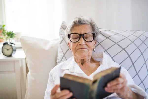 Sick senior woman with glasses reading bible in bed at home or in hospital. — Stock Photo, Image