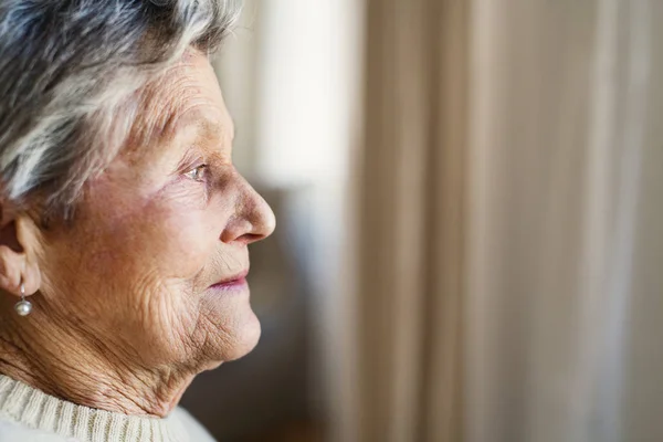 Szczegół portret senior kobiety w domu, patrząc z okna. — Zdjęcie stockowe