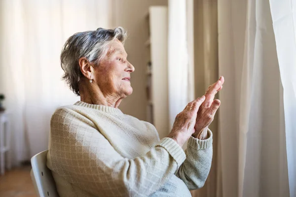 Porträt einer Seniorin, die zu Hause sitzt und aus dem Fenster schaut. — Stockfoto