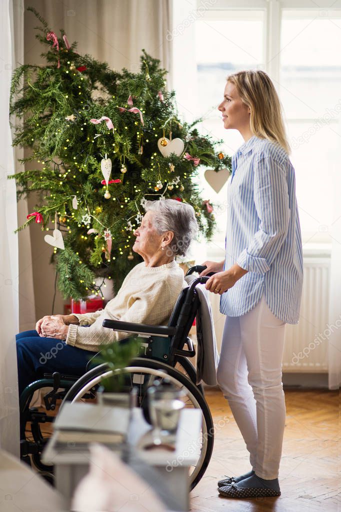 A senior woman in wheelchair with a health visitor at home at Christmas time.