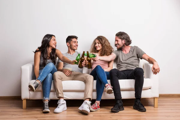 Retrato de un grupo joven de amigos sentados en un sofá en un estudio, tintineando botellas . — Foto de Stock