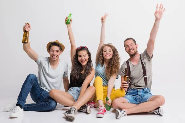 Portrait of joyful young group of friends with bottles sitting on the ground in a studio. — Stock Photo, Image