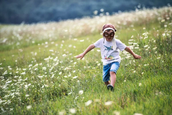 Um menino pequeno com óculos de piloto e chapéu correndo na natureza em um dia de verão . — Fotografia de Stock