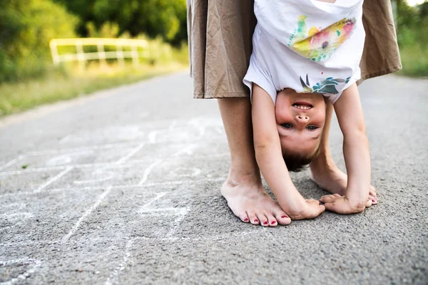 Oigenkännlig mor hålla en liten son upp och ned på en väg i park i sommar. — Stockfoto