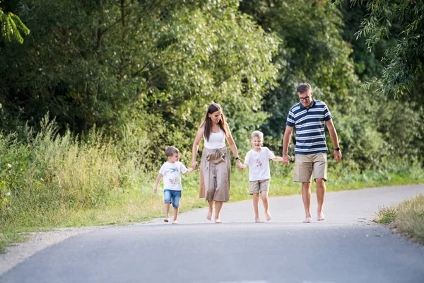 Eine Familie mit zwei kleinen Söhnen, die an einem Sommertag barfuß auf einer Straße im Park läuft. — Stockfoto