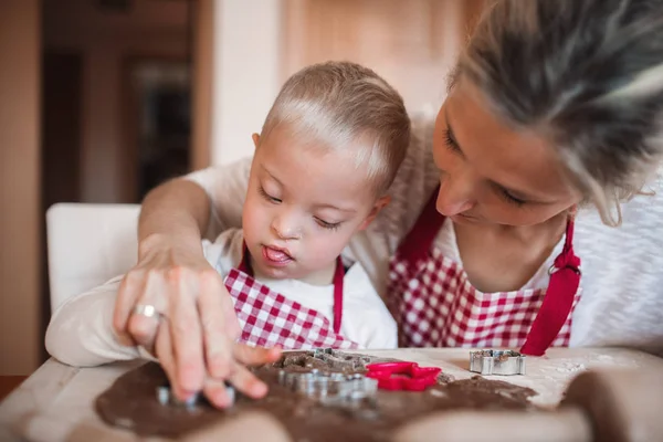 Een gehandicapte Downsyndroom jongen met zijn moeder binnenshuis bakken. — Stockfoto