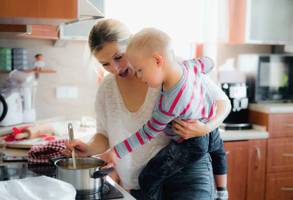Vaření polévky se svou matkou doma postižené Downovým syndromem chlapec. — Stock fotografie