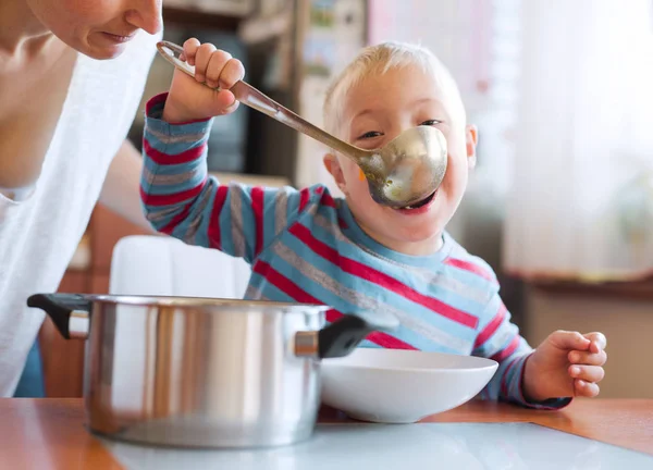 屋内では、鍋からスープを食べる障害ダウン症少年昼食の時間. — ストック写真