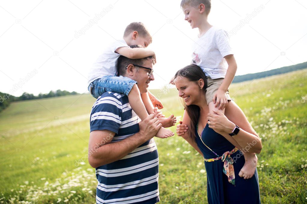 A father and mother giving piggyback ride to small sons in nature on a summer day.