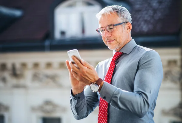 Mogen affärsman med smartphone som står på en terrass i city, textning. — Stockfoto