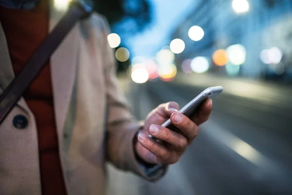 Mittelschnittansicht eines Geschäftsmannes mit Smartphone, der abends auf einer Straße steht. — Stockfoto