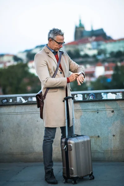 Mogen affärsman med resväska står på en bro i Prague city. — Stockfoto