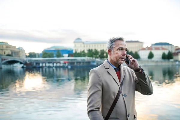 スマート フォン プラハ シティのヴルタヴァ川のそばに立って、成熟したビジネスマン. — ストック写真