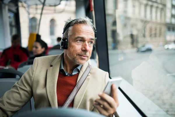 Зрілий втомлений бізнесмен з хефонами і смартфон подорожуючи на автобусі в місті . — стокове фото