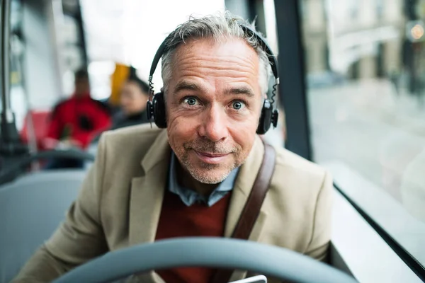 Mature tired businessman with heaphones travelling by bus in city. — Stock Photo, Image