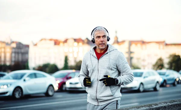 ヘッドフォンの屋外を実行するプラハ市内の橋の上で成熟した男性ランナー. — ストック写真