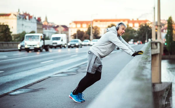 Volwassen mannelijke atleet met koptelefoon rekken buiten op de brug in Praag stad. — Stockfoto