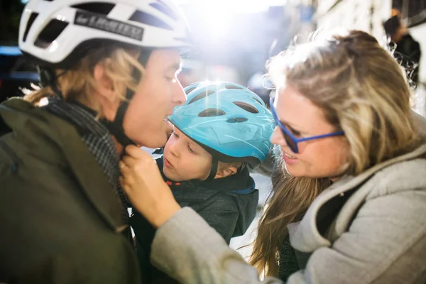 Un piccolo bambino con casco e giovani genitori all'aperto in città . — Foto Stock