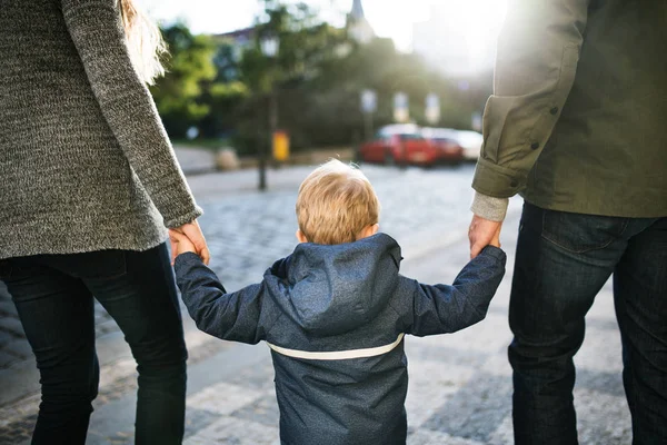 A rear view of small toddler boy with unrecognizable parents walking outdoors in city. — Stock Photo, Image