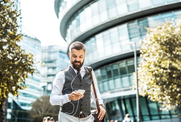 Hipster businessman with smartphone and earphones walking on the street. — Stock Photo, Image