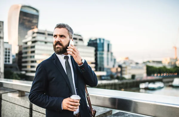 Hipster hombre de negocios con café y smartphone de pie al aire libre en la ciudad . —  Fotos de Stock