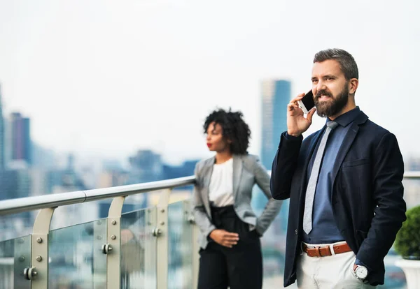 Um retrato de um homem de negócios com smartphone em pé em um terraço . — Fotografia de Stock