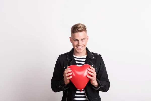 A young man in a studio, holding red heart balloon in front of him. — Stock Photo, Image