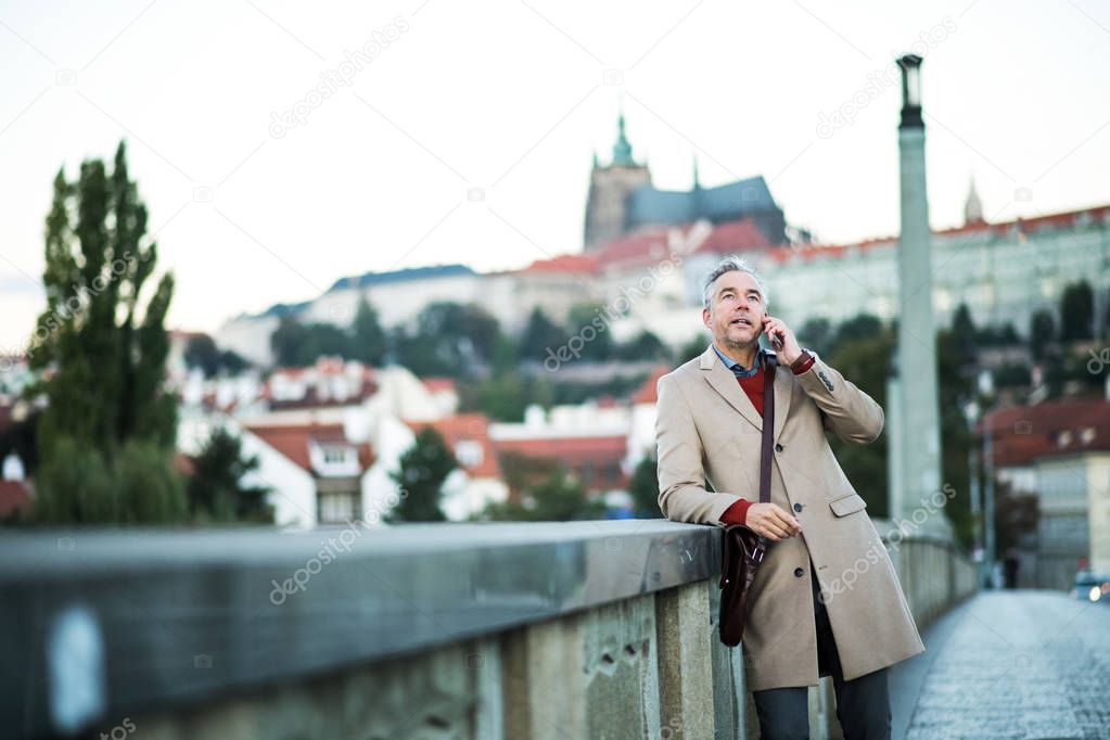 Businessman with smartphone standing on a bridge in city, making a phone call.