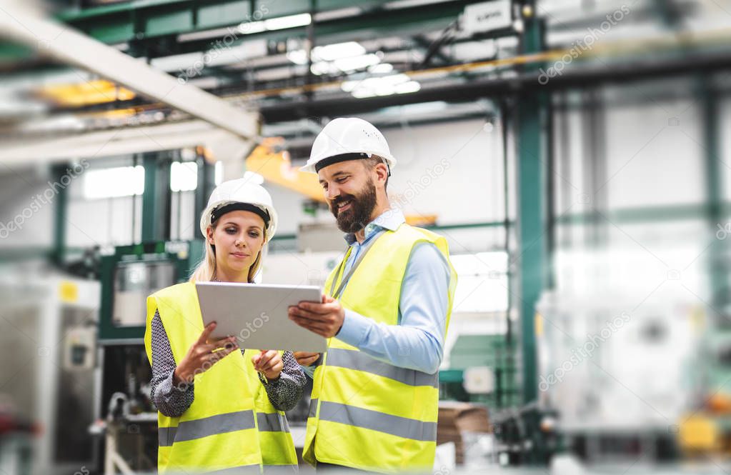 A portrait of an industrial man and woman engineer with tablet in a factory, talking.