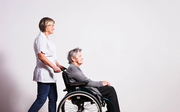 Студийный портрет пожилой женщины в инвалидной коляске и медсестры . — стоковое фото