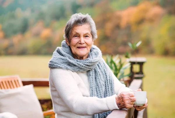 Uma mulher idosa de pé ao ar livre em um terraço em um dia ensolarado no outono . — Fotografia de Stock