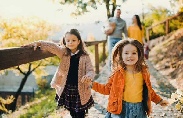 Dua gadis dengan orang tua yang tak dikenal berjalan di taman di musim gugur . — Stok Foto