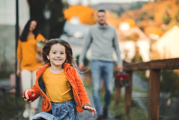 Small girl with unrecognizable parents in the background running in park in autumn. — Stock Photo, Image