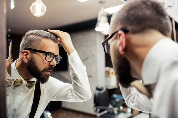 Hipster-Mann mit Brille schaut in Friseurladen in den Spiegel. — Stockfoto