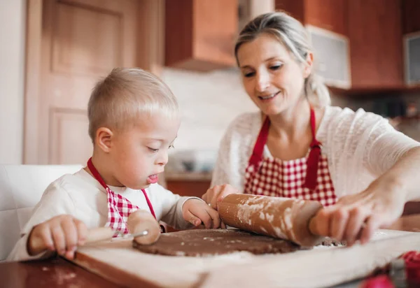 A handicapped down syndrome child with his mother indoors baking. — Stock Photo, Image
