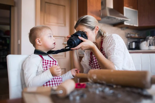 障害ダウン症の少年と彼の母親を焼くとき デジタル カメラで写真を撮ってキッチンで室内 — ストック写真