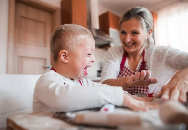 Un niño con síndrome de minusvalía riendo con su madre en el interior horneando . —  Fotos de Stock