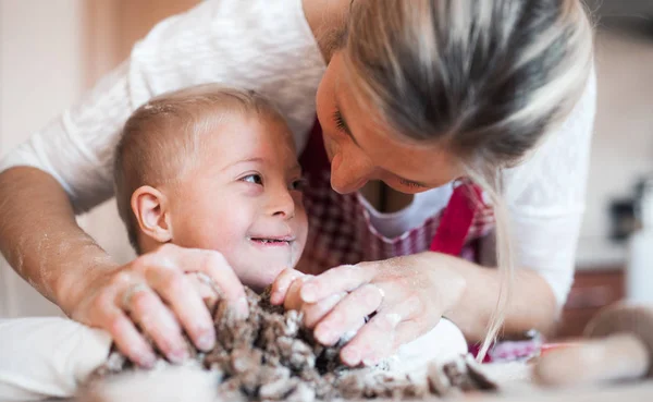 Un niño con síndrome de minusvalía feliz con su madre en el interior horneando . —  Fotos de Stock