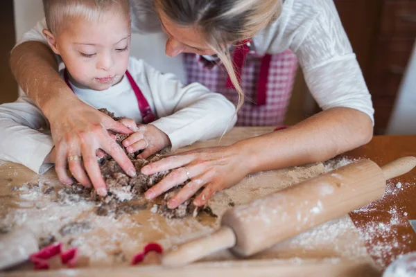 A happy handicapped down syndrome child with his mother indoors baking. — Stock Photo, Image